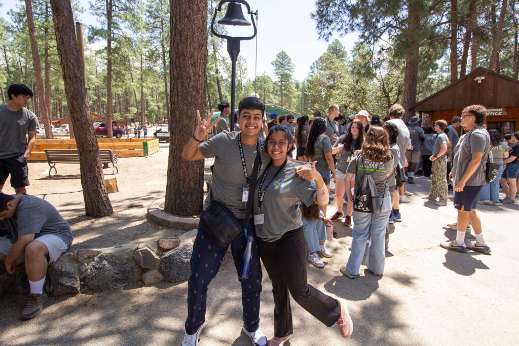 Two students stand before a crowd of first year ASU Engineering students, smiling for the camera and making the ASU pitchfork school spirit gesture.