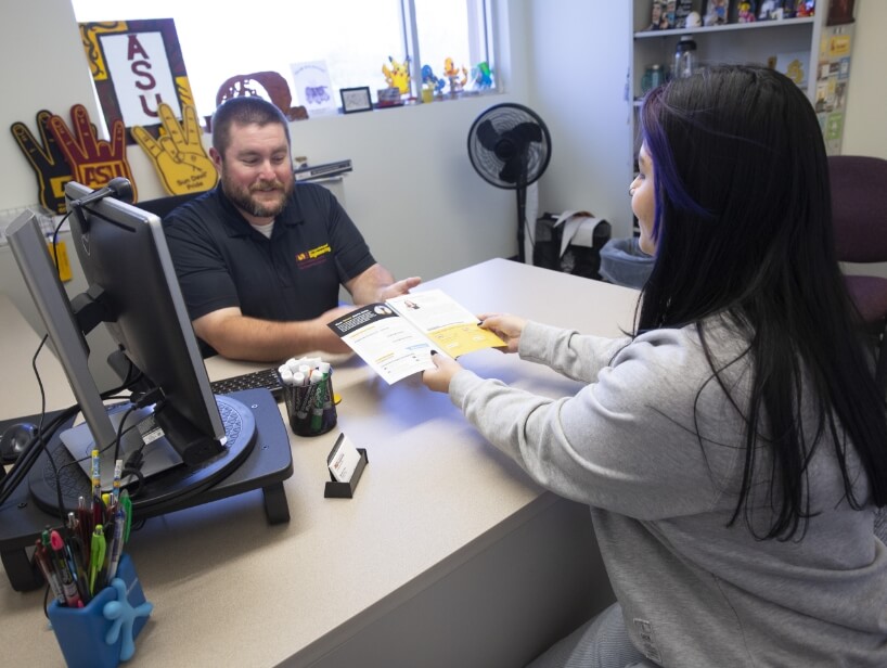 An adviser chats with a student across a desk