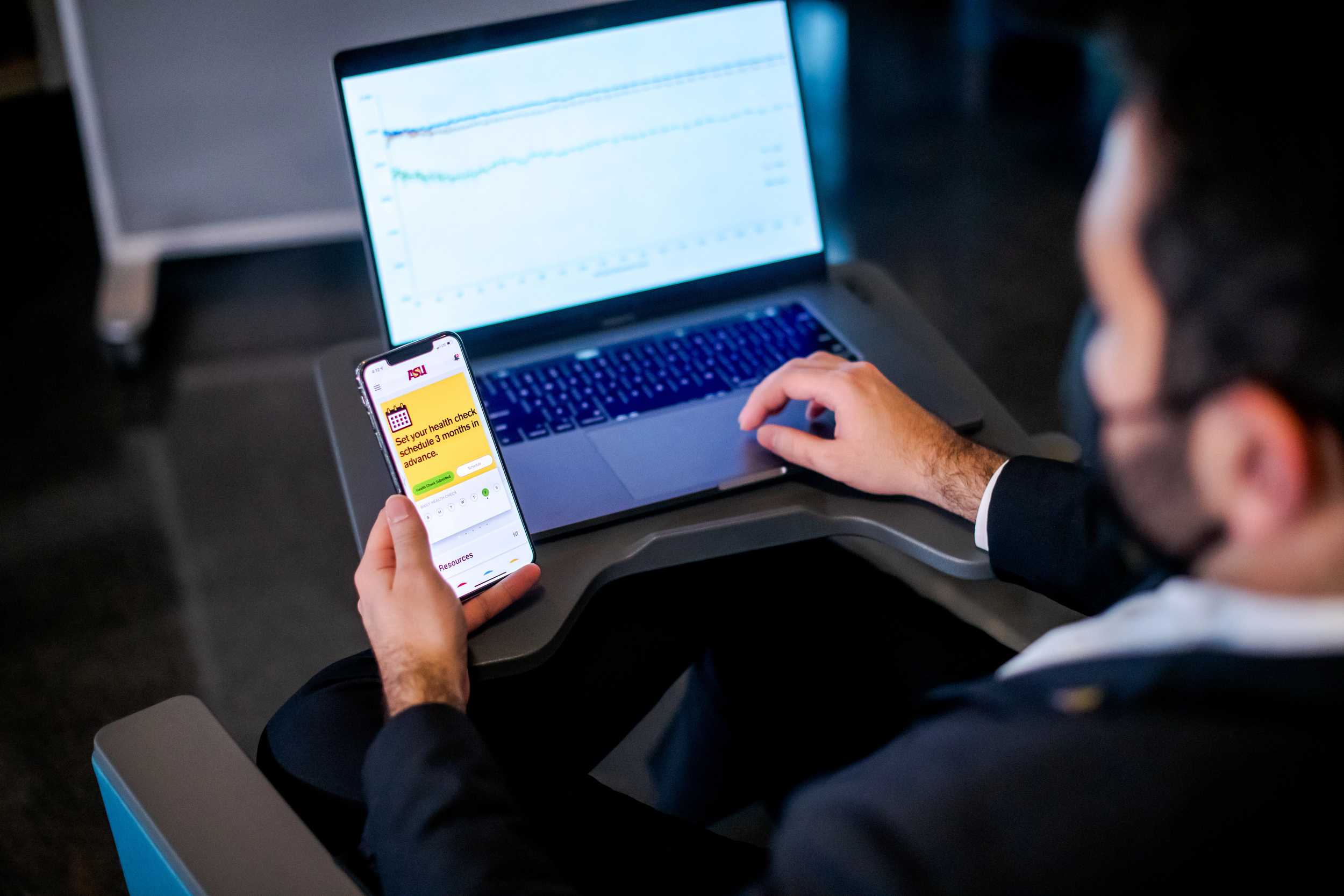 A man works at a laptop while also checking something on his phone
